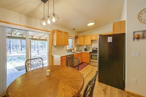 Una cocina con armarios de madera, un refrigerador de acero inoxidable, una mesa de comedor con sillas y vistas a través de la puerta de vidrio.