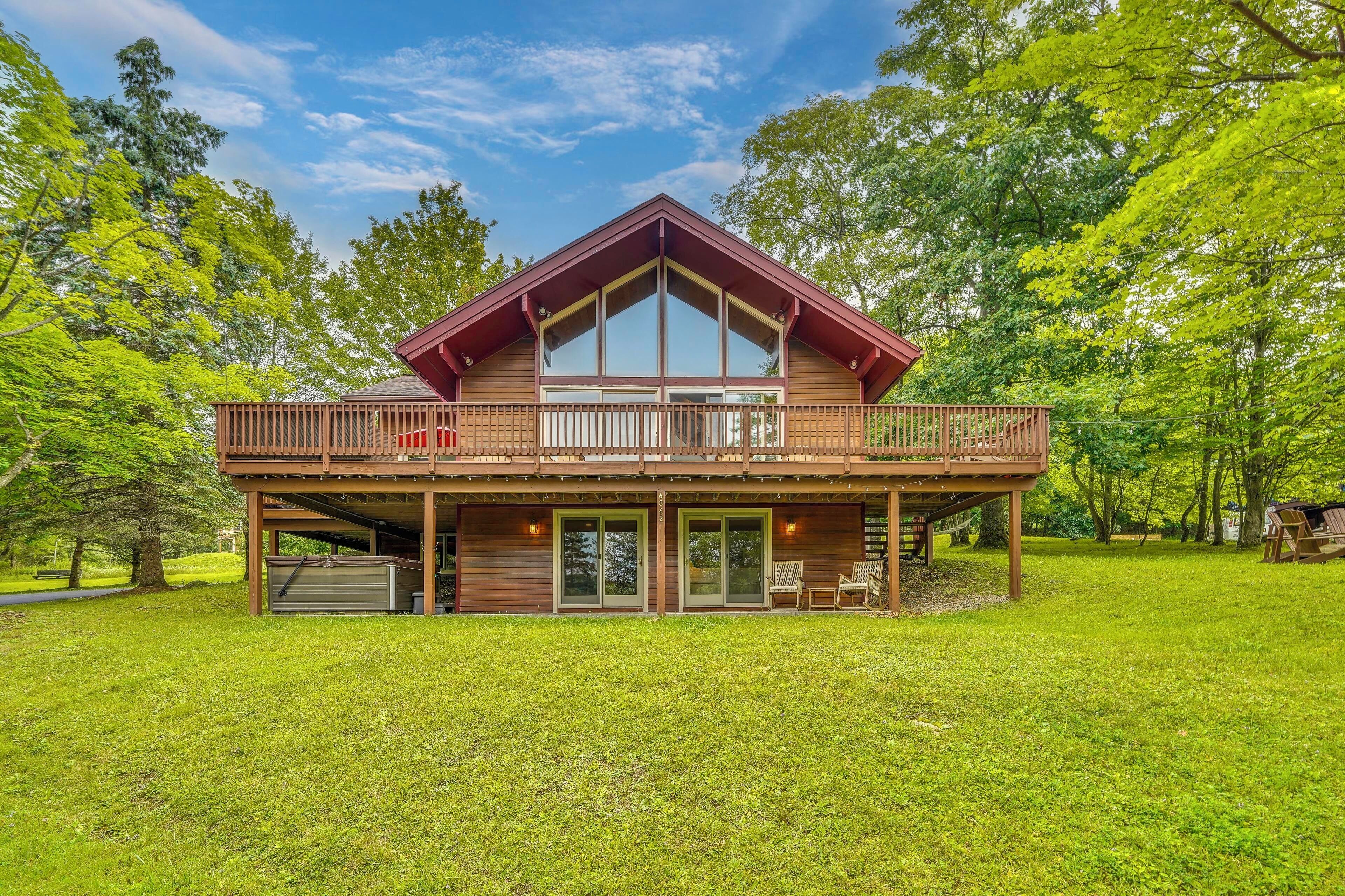 A two-story wooden house with a balcony, large windows, and a covered patio area.