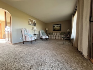 A living room with a carpeted floor, two armchairs, a sofa, a coffee table, and two lamps.