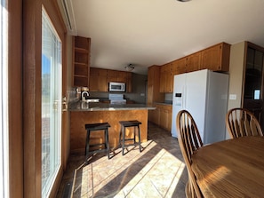 A kitchen with wooden cabinets, a white refrigerator, a microwave, and a dining area with a table and chairs.