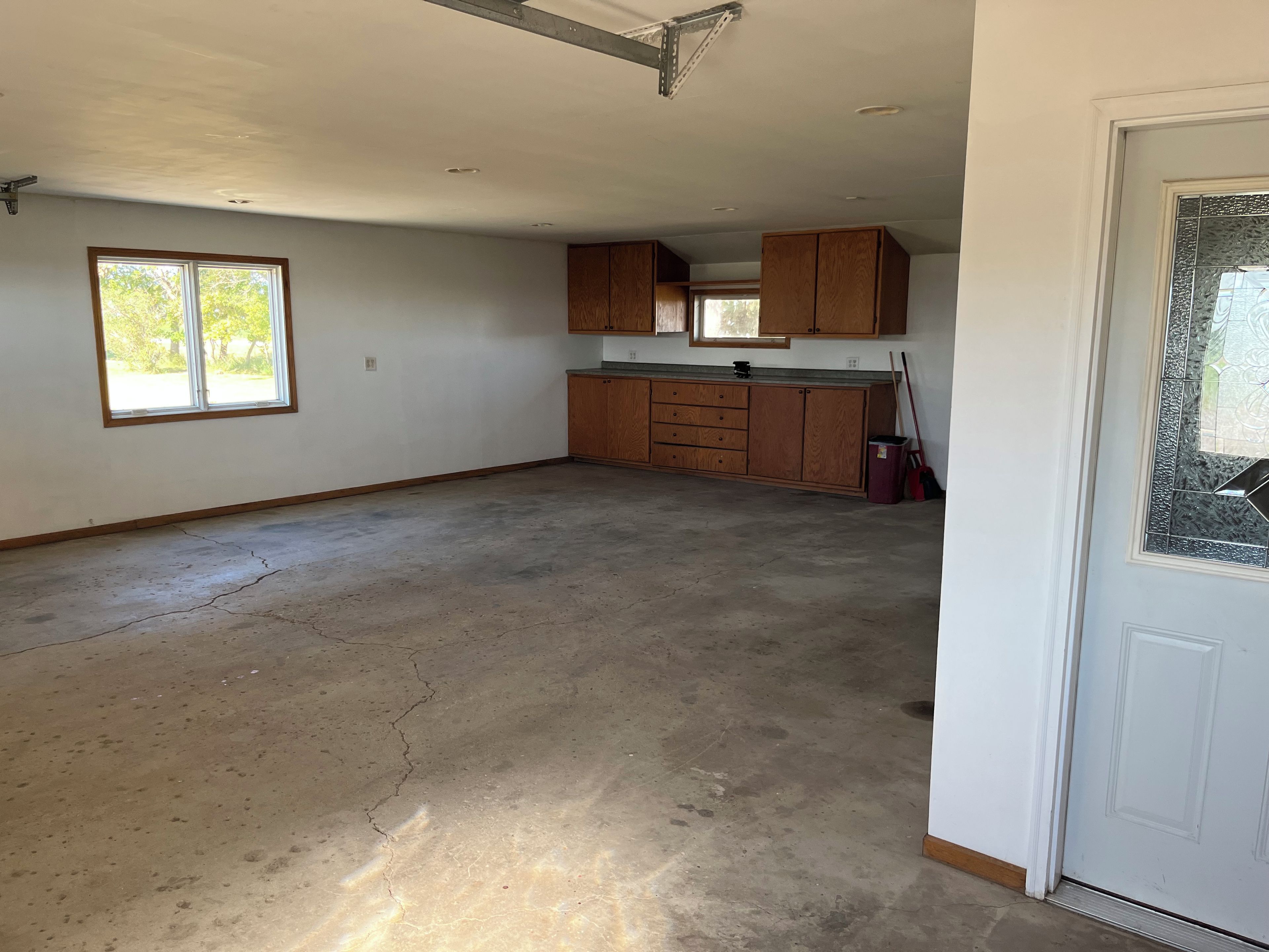 A spacious room with a large window, a kitchen area with wooden cabinets, and a concrete floor.