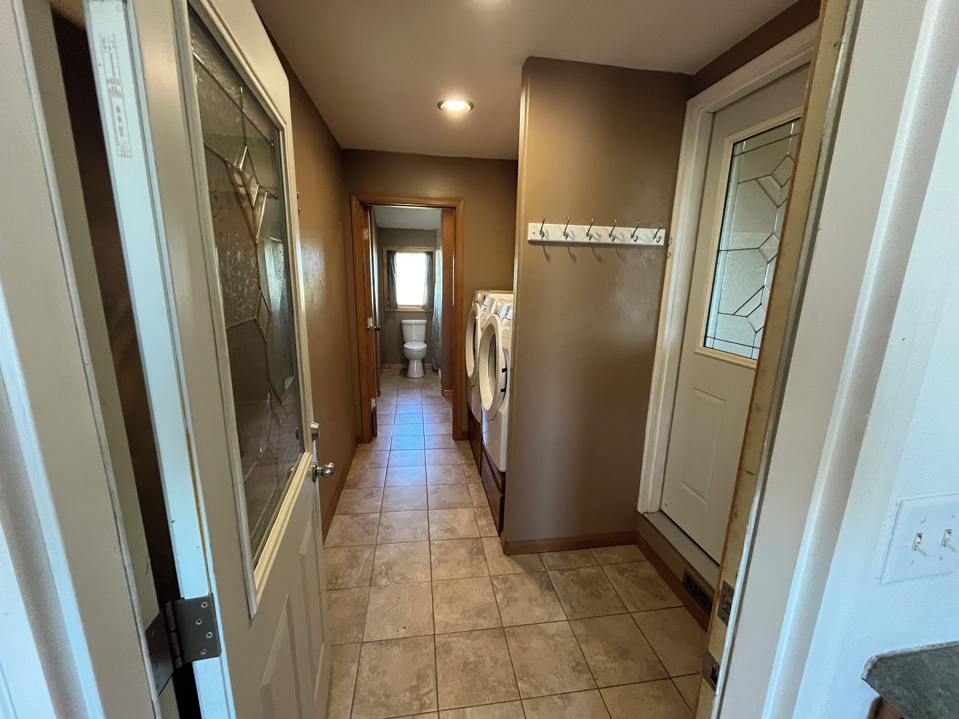 A hallway with a washing machine, a door with a glass panel, and a tiled floor.