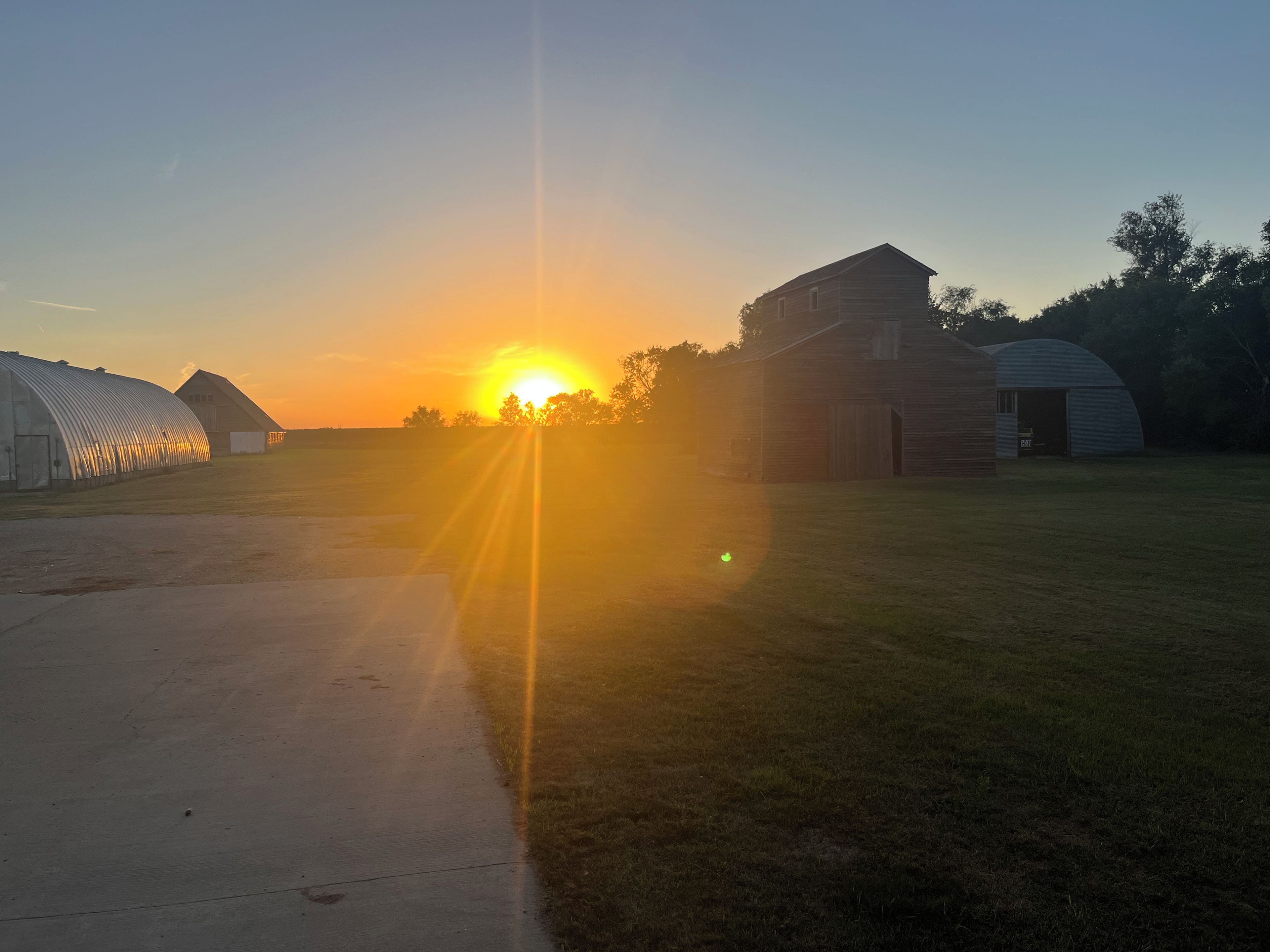 A sunset over a rural landscape with barns and a greenhouse.