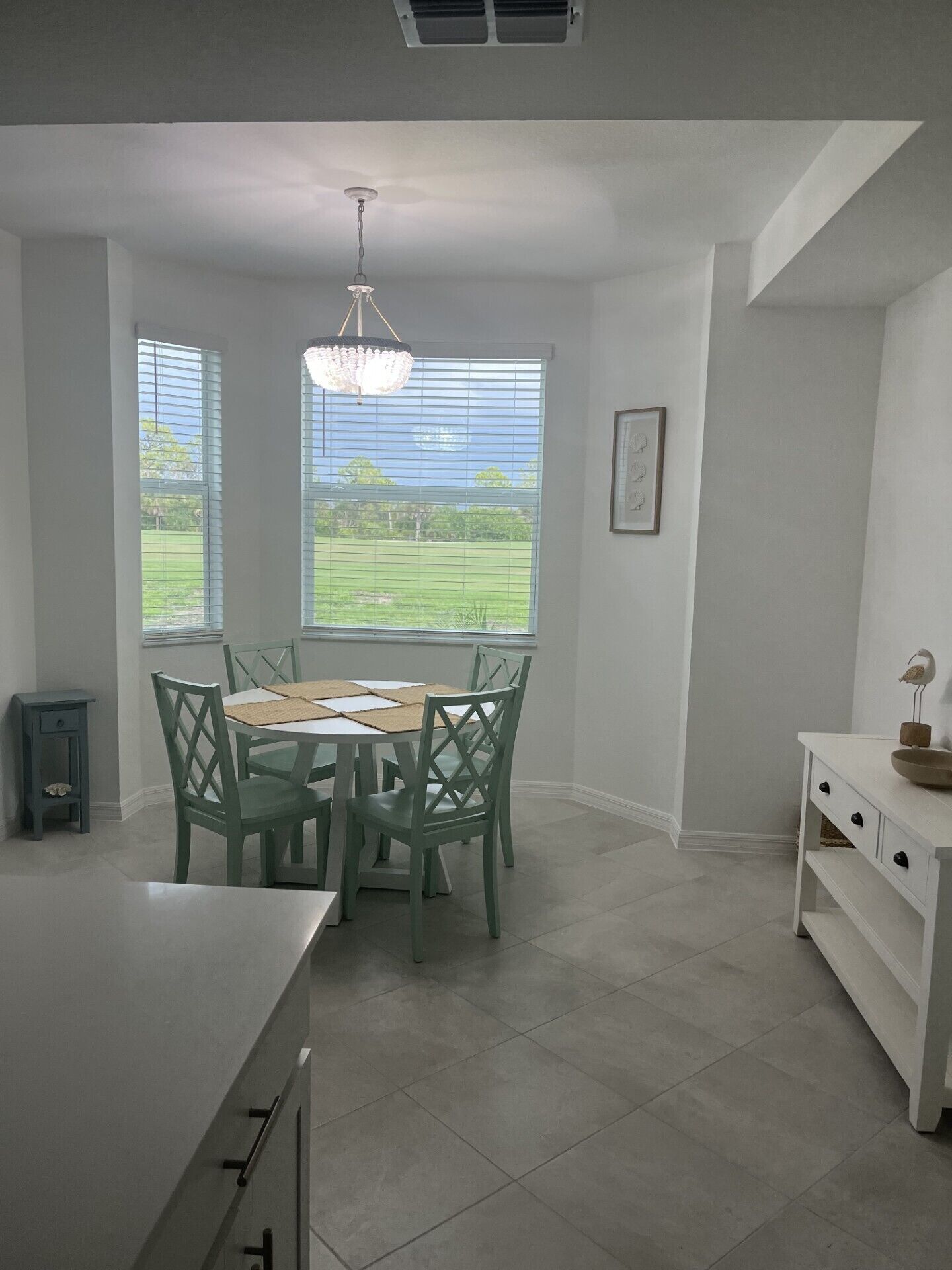 A kitchen with a dining table and chairs, a chandelier, and large windows with a view of greenery.