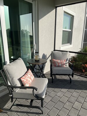 A patio with two chairs and a small table, a glass door, and a window with blinds. - Coastal Feel  Wellen Park G&CC condo (Venice)