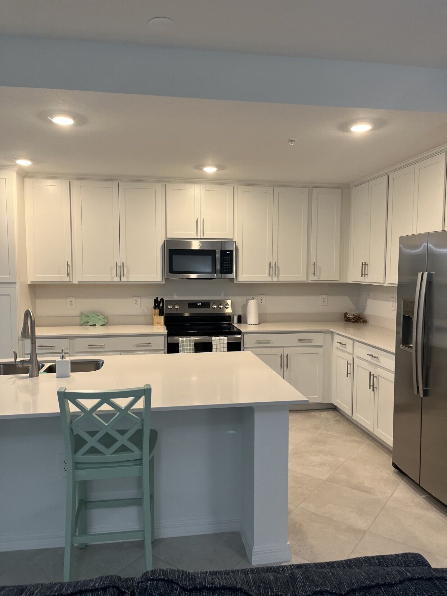 A modern kitchen with white cabinets, stainless steel appliances, and a central island with a chair.