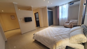A modern bedroom with a large bed, a flat-screen TV, and a seating area with a massage chair.