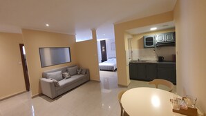 A modern living room with a sofa, a dining table, and a kitchen area with cabinets and a sink.
