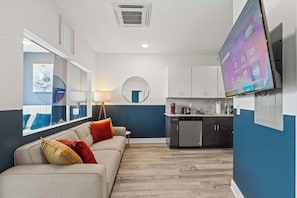 A modern living room with a sofa, a round mirror, and a television mounted on the wall. - Modern 2BR | Sleeps 6 | Northern Liberties (Philadelphia)
