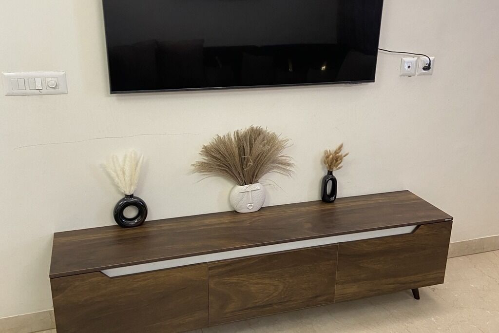 A modern living room with a flat-screen TV mounted on the wall, a wooden console table with decorative vases, and a wall socket.