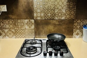 A kitchen with a gas stove, a frying pan, and a wall with patterned tiles. - Spacious 3-bedroom apartment with AC in cool Gurugram (Gurugram)