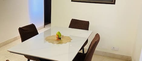 Un comedor con una mesa blanca, cuatro sillas marrones y una pequeña figura de pájaro verde sobre la mesa.