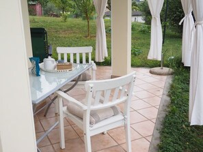 A patio with a glass table and white chairs, a kettle, and a small table with a teapot.