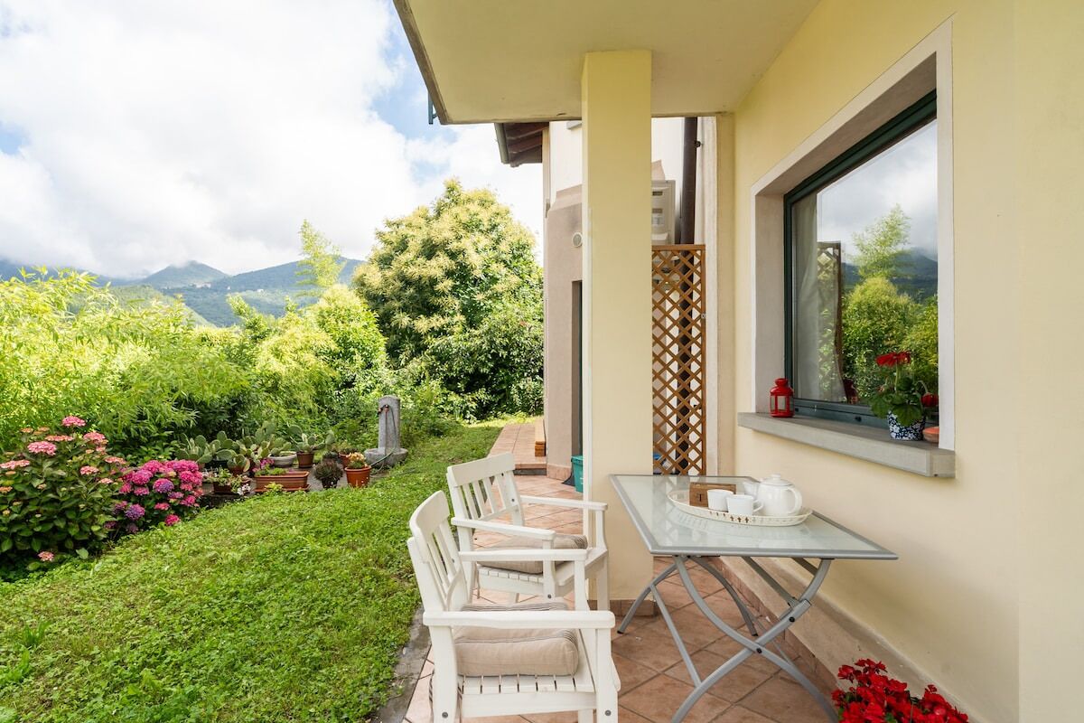 A patio with two white chairs and a table, a window with a view of greenery and mountains, and a small shelf with red lanterns.