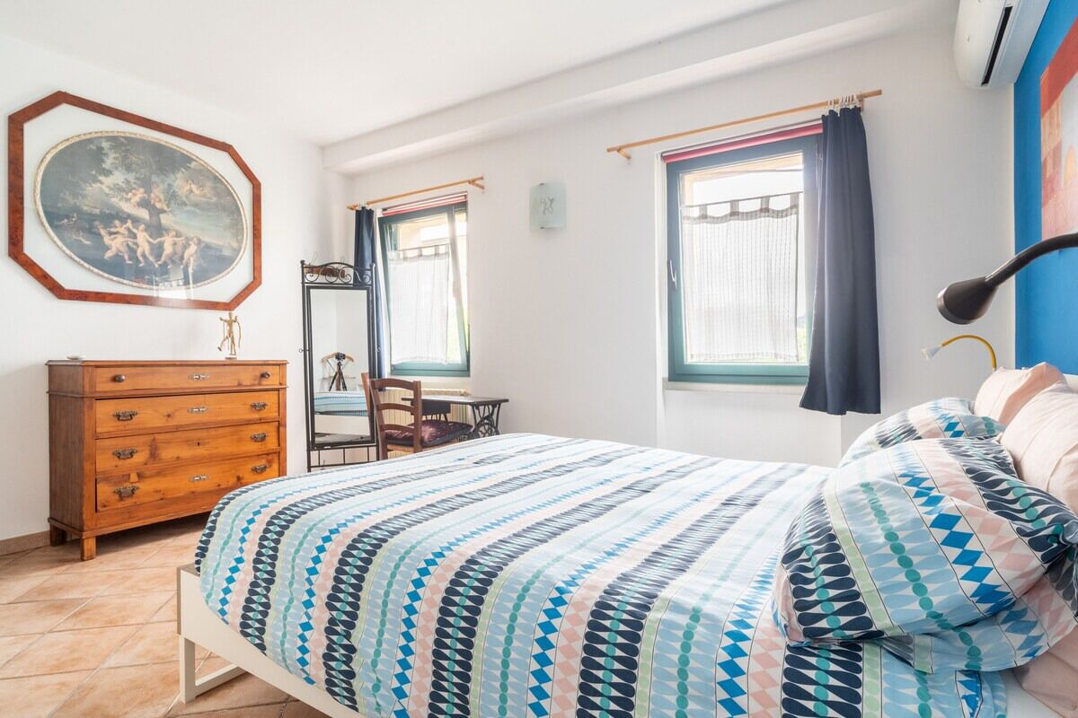 A bedroom with a bed, dresser, chair, and a painting on the wall.