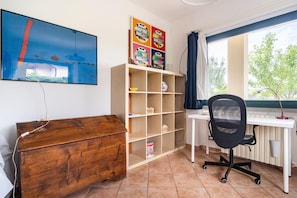 A room with a wooden desk, a chair, a bookshelf, and a painting on the wall.