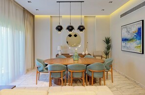 Uma sala de jantar com uma mesa redonda, seis cadeiras, um vaso e um quadro na parede.