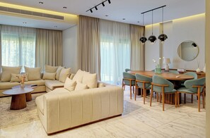 Ein modernes Wohnzimmer mit Sofa, Couchtisch, Esstisch mit Stühlen und einem großen Spiegel an der Wand.