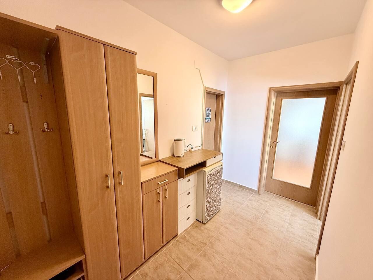 Ein Zimmer mit einem Holzschrank, einer kleinen Ablagefläche mit Wasserkocher und einer Tür mit Milchglasverglasung.