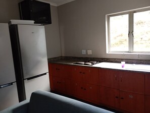 A kitchen with a refrigerator, a microwave, a window, and a sink. - Groups Accommodation (Durban)