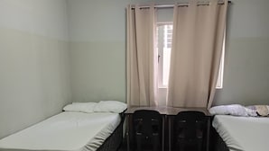 A small, single-room accommodation with two single beds, a table, two chairs, and a window with curtains. - Groups Accommodation (Durban)