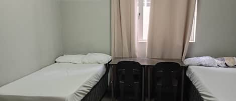 Un alojamiento pequeño y de una sola habitación con dos camas individuales, una mesa, dos sillas y una ventana con cortinas.