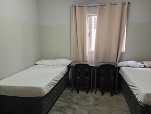 A small, single-room accommodation with two single beds, a table, two chairs, and a window with curtains. - Groups Accommodation (Durban)
