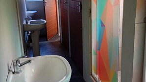 Une salle de bain avec un lavabo blanc, un miroir et une fenêtre. Une porte ornée d’un motif géométrique coloré se trouve sur le mur.