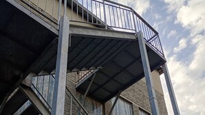 Une structure d’escalier métallique à plusieurs niveaux, dotée de rampes, menant à un bâtiment à la façade en briques.