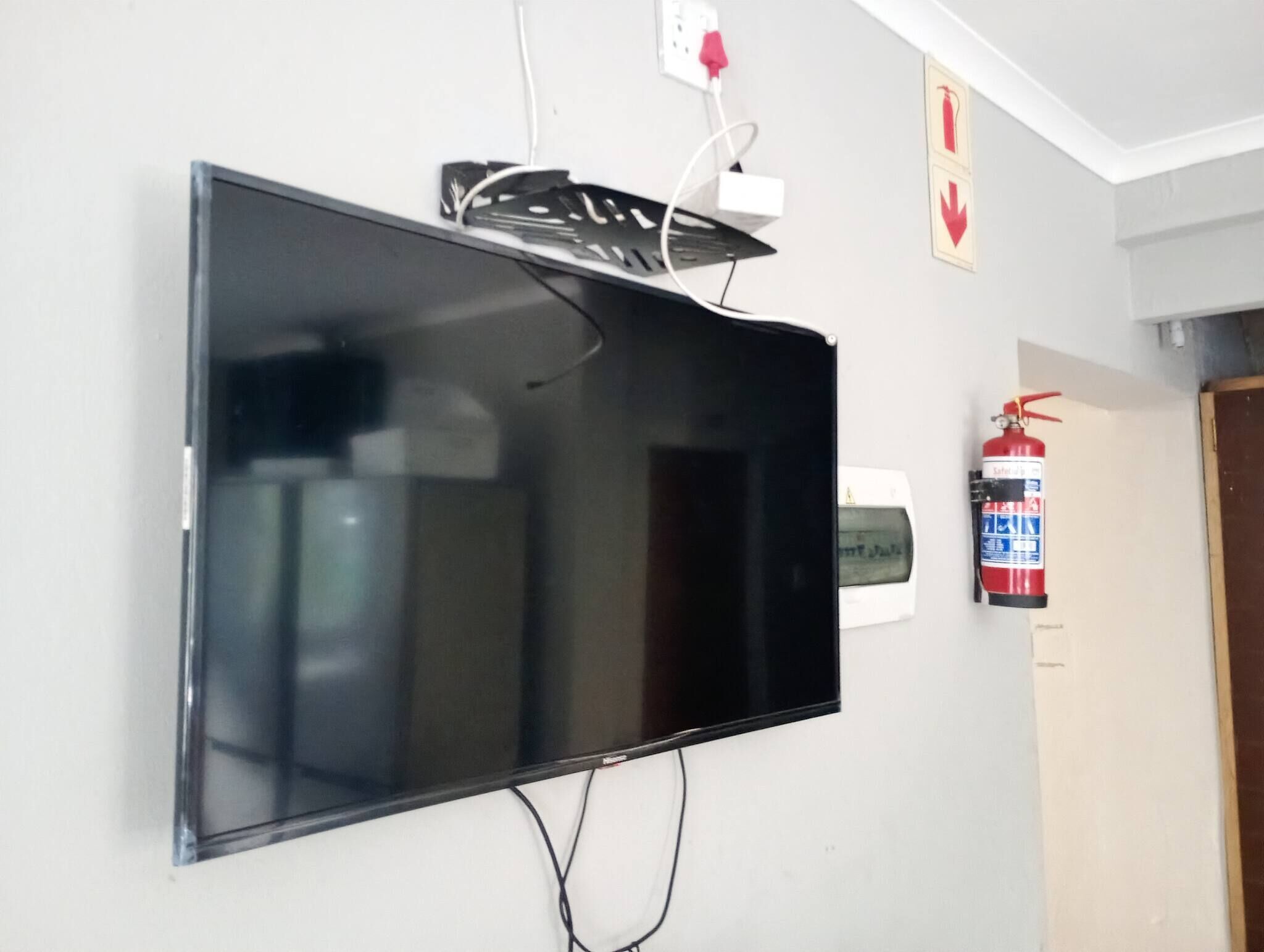 Un televisor de pantalla plana montado en la pared, con un enchufe y un extintor cerca.