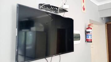 Un televisor de pantalla plana montado en la pared, con un enchufe y un extintor cerca.