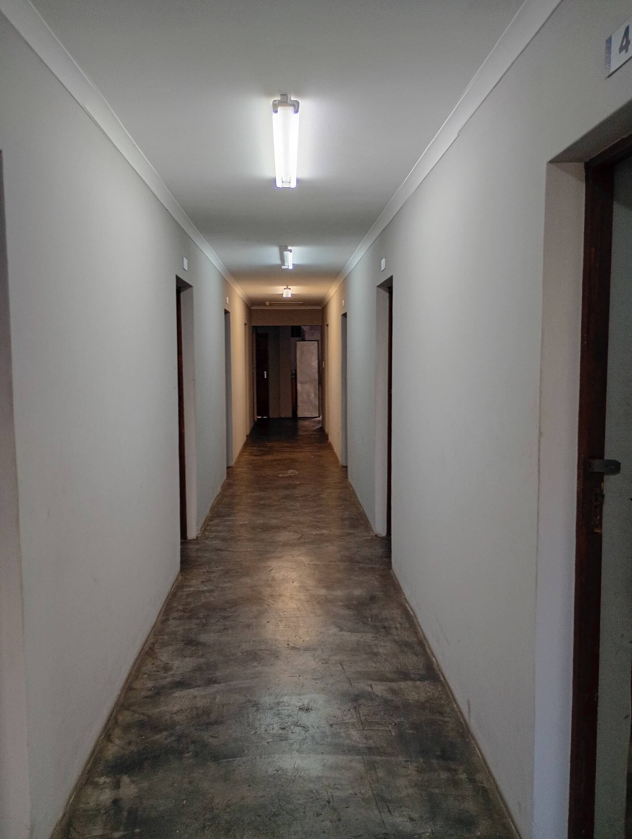 A narrow hallway with a wooden floor, white walls, and a ceiling light fixture.