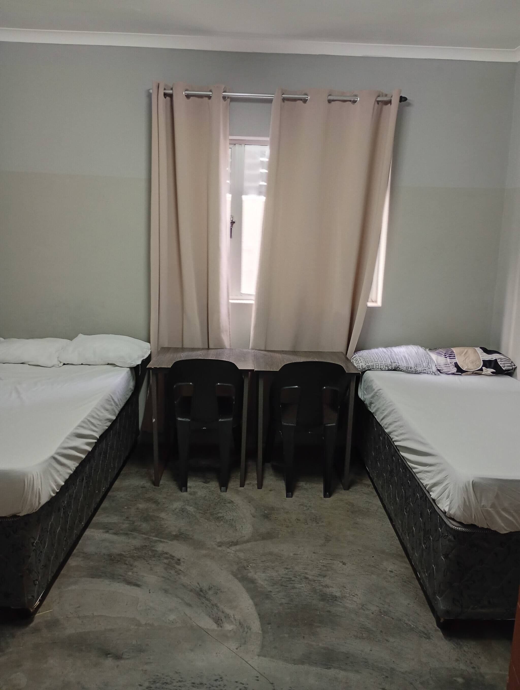 Une chambre avec deux lits, une petite table et deux chaises.