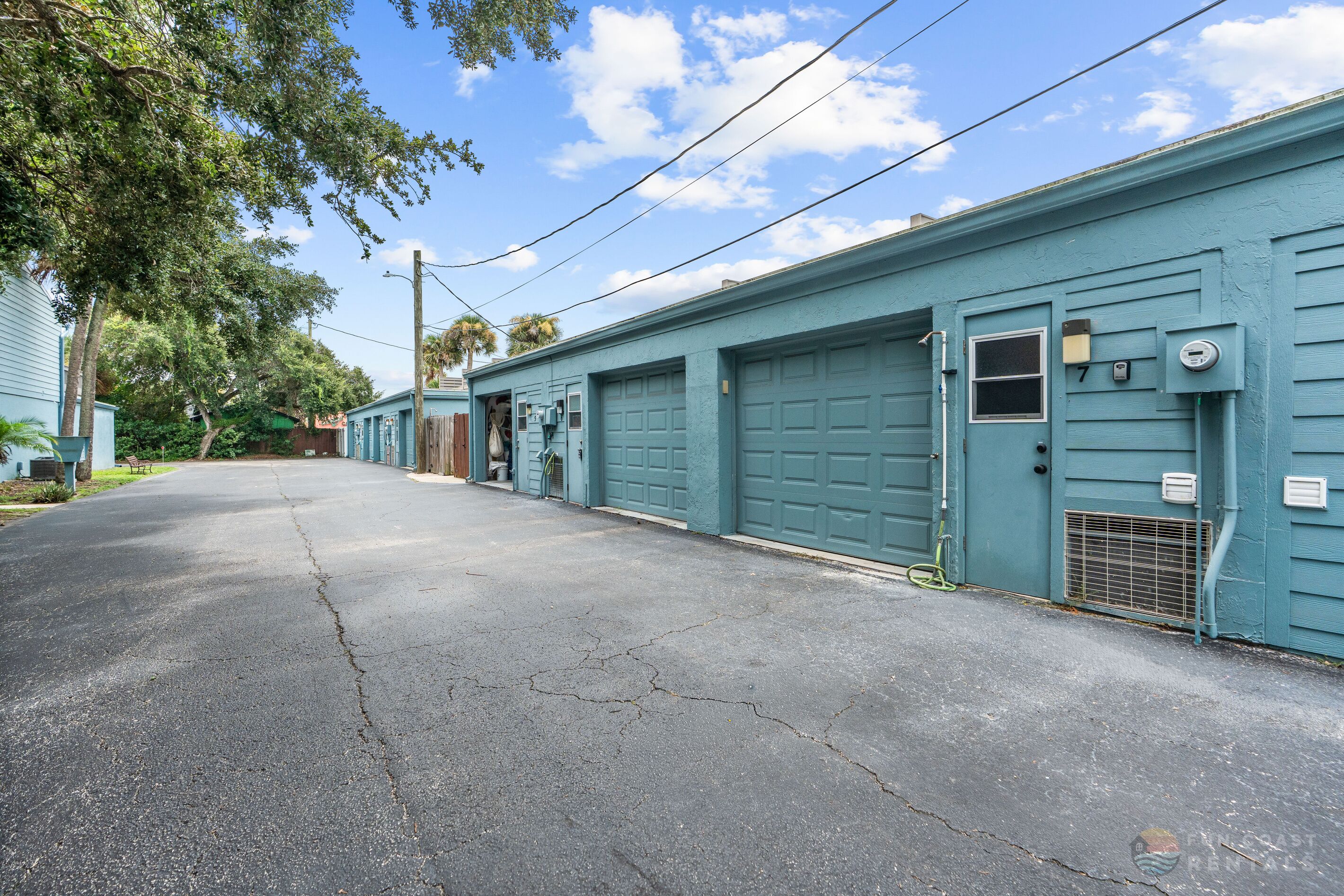 A row of light blue buildings with garage doors, a clear sky, and a paved street.