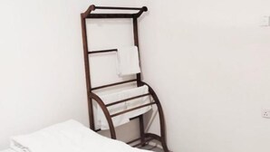 Una stanza dall'aspetto clinico con un letto, un mobiletto in legno con asciugamani e un condizionatore d'aria a parete.