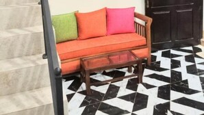 Una scala con ringhiera nera conduce a un pianerottolo. Sotto, una panca in legno con piano in vetro si trova di fronte a un pavimento a scacchi bianco e nero. In secondo piano si nota una porta in legno scuro.