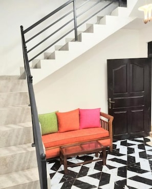 A staircase with a black handrail leading to a landing. Below, a wooden bench with a glass top is positioned in front of a black and white checkered floor. A dark wooden door is visible in the background. - Cozy Home Stay - Wonderful 3-bedroom house with AC and with complete privacy (Wattala)