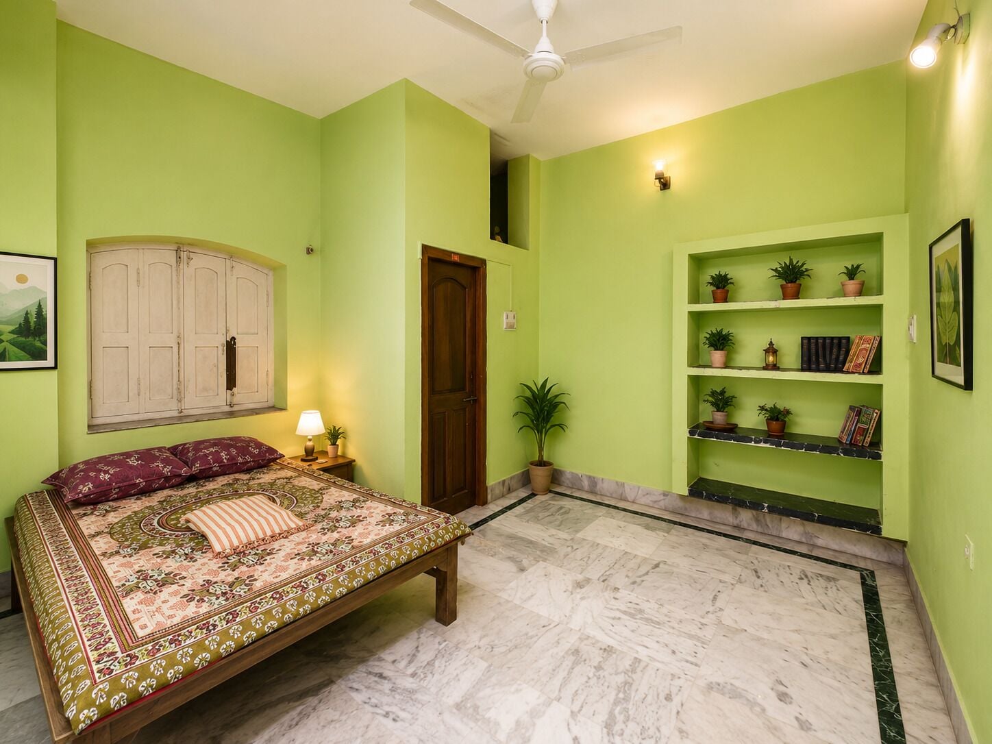 Une chambre à coucher avec un lit, une table de chevet, une lampe, une porte, une étagère avec des plantes et un tableau encadré au mur.