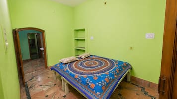 Una habitación con cama, puerta, estante y alfombra estampada.