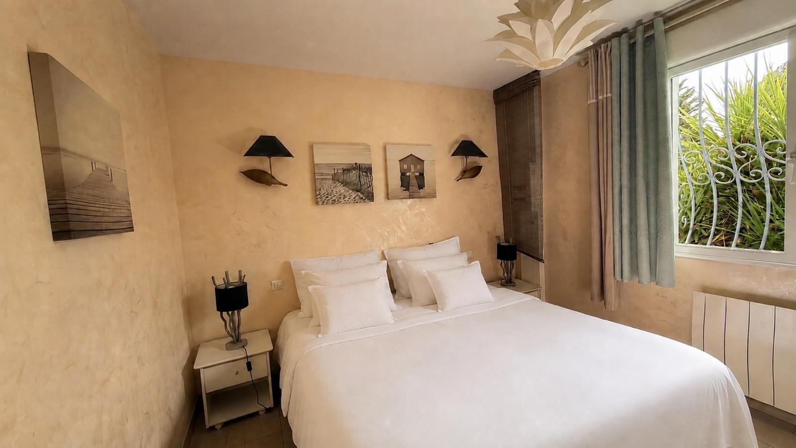 A hotel room with a large bed, two bedside tables with lamps, and artwork on the walls.