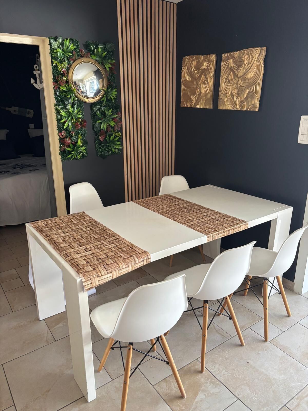 Comedor con una mesa blanca, cuatro sillas blancas, un mantel tejido, un espejo y decoración mural.