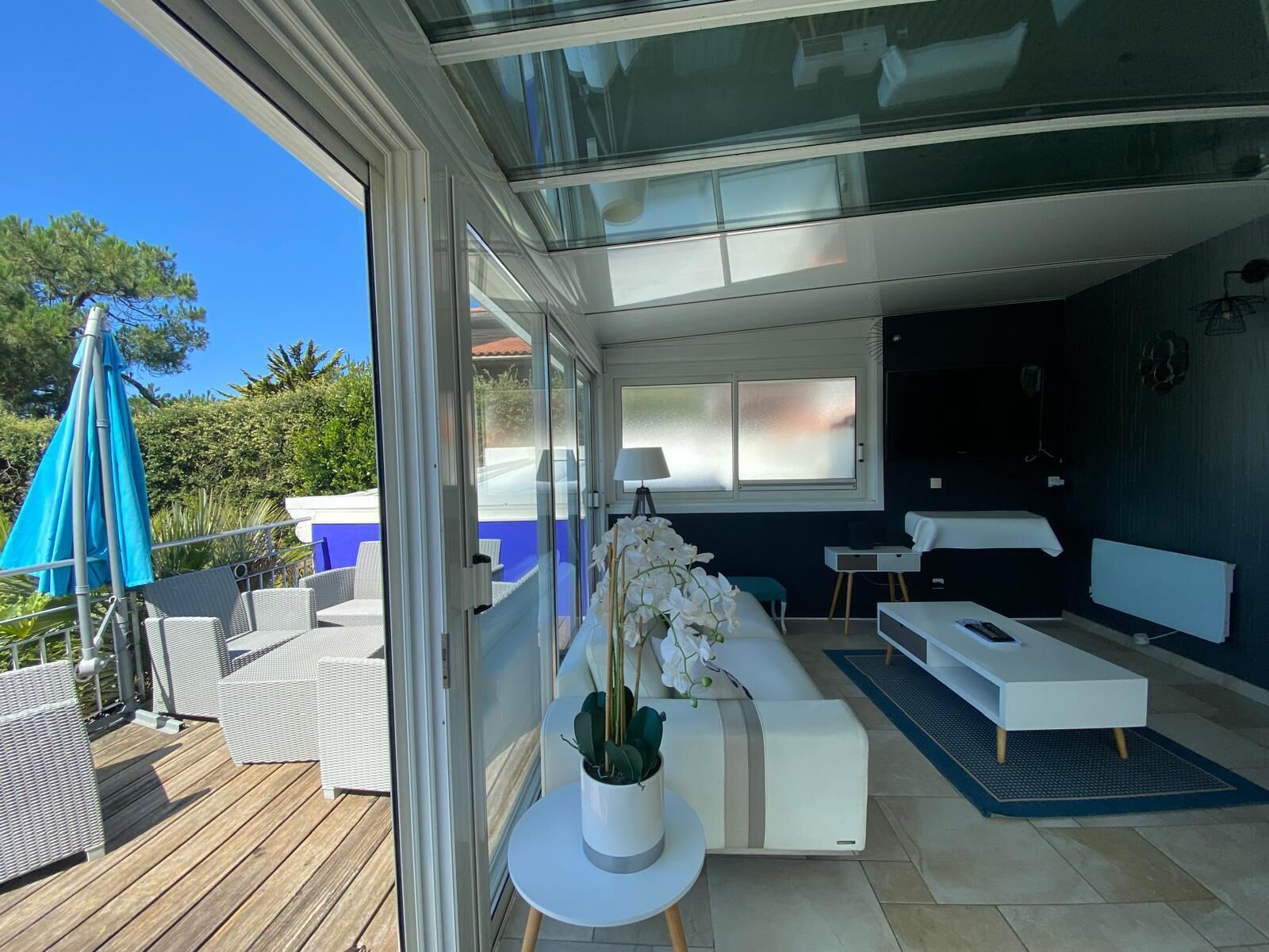 A modern interior with a glass door leading to an outdoor area, a white sofa, a small table with a lamp, and a potted plant.
