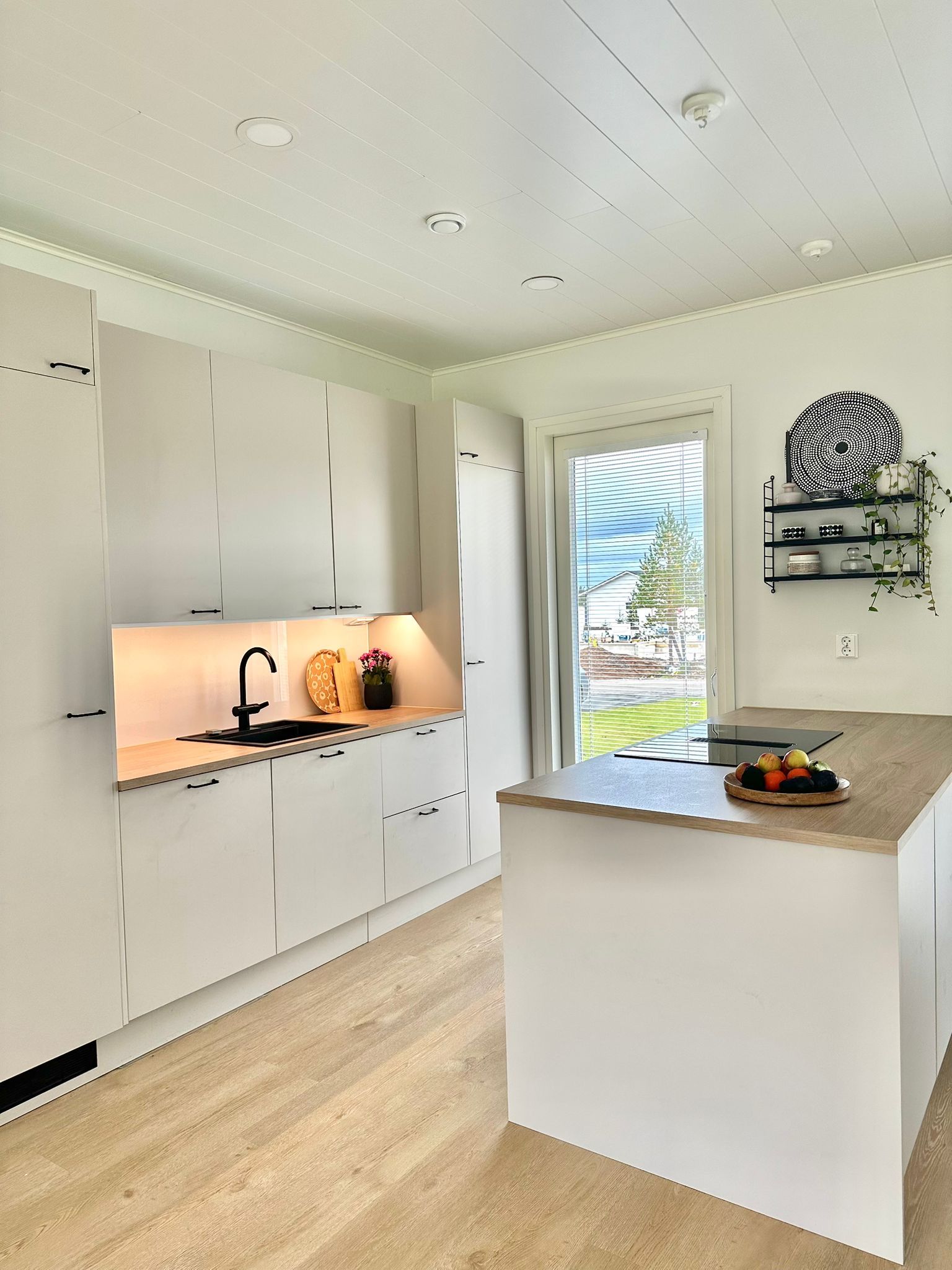 A modern kitchen with white cabinetry, a central island, and a window with blinds.