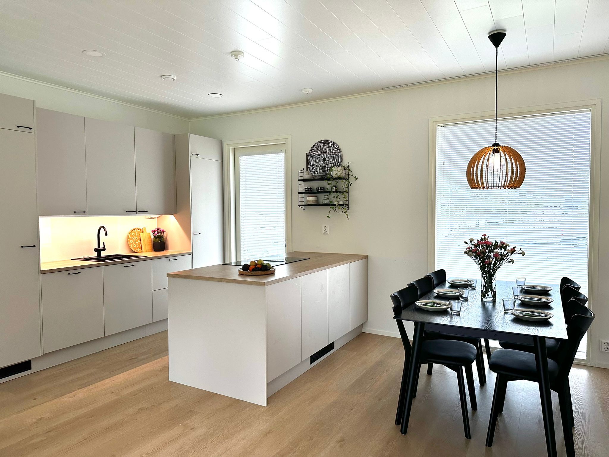 Una cocina moderna con armarios blancos, una isla central y un comedor con mesa y sillas.