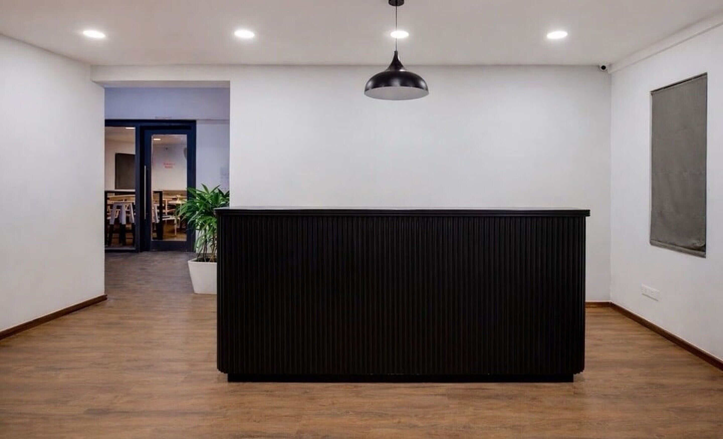 A reception desk in a modern interior with a wooden floor, a black panel, and a hanging pendant light.