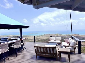 Une terrasse extérieure avec des sièges et un espace barbecue, offrant une vue sur un paysage côtier.