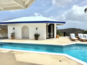 Un espace aménagé au bord de la piscine, avec un bâtiment blanc, deux chaises longues et une vue sur un paysage vallonné.