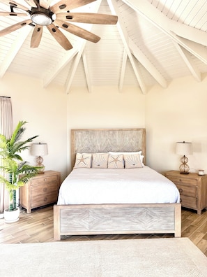 Una camera da letto con un letto in legno, due comodini, una ventola a soffitto e un'ampia finestra.