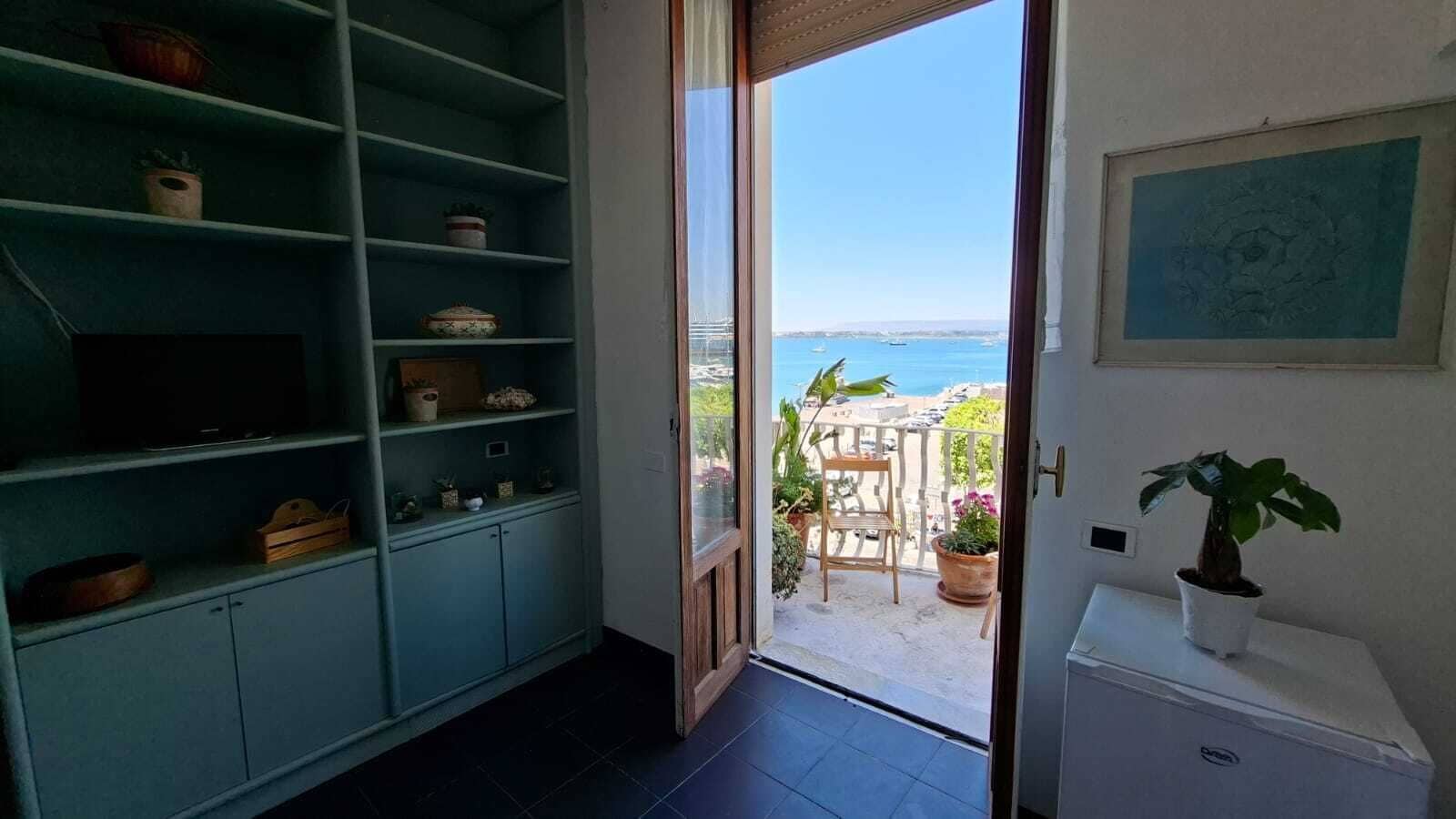 A room with a view of the sea, a wooden chair, and a potted plant.