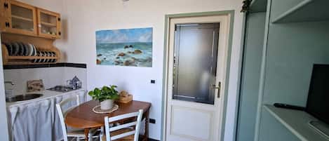 A compact kitchen with a dining table, a stove, and a sink. There is a door with a frosted glass panel and a small plant on the table.